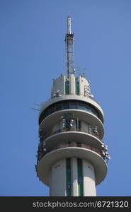 A telecommunication tower in a clear blue sky, showing loads of antennas and satelite connections