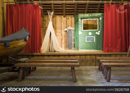 A theater at a summer camp that is used for occasional performances. The stage has a few props including a teepee, a booth, and a boat for use by the actors.