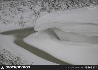 a thick layer of snow overhanging an almost frozen ditch during the winte rin holland