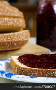 A thick layer of tangy raspberry jam, on whole wheat multi-grain bread. Focus on bread.