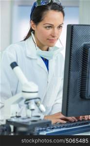 A thoughtful female medical or scientific researcher or woman doctor using a computer in a laboratory with microscope and other equipment in the foreground.