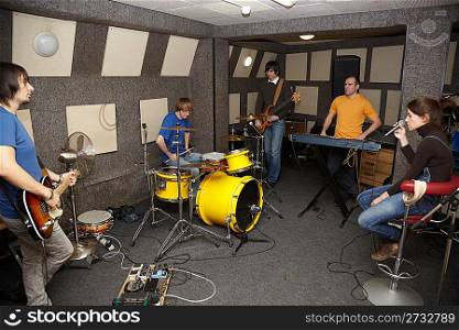 a thoughtful rock band. sad vocalist girl, two musicians with electro guitars and one drummer working in studio.