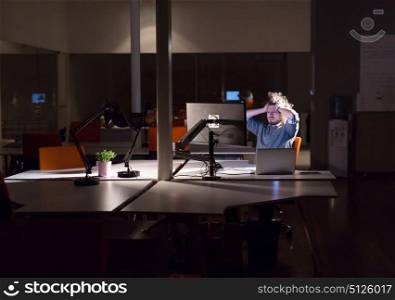 A time for relax. Young tired casual businessman relaxing at the desk in his night office