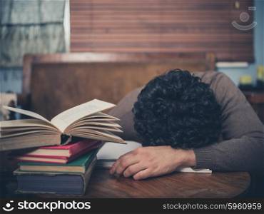 A tired student is asleep with his head on a coffee table surrounded by books