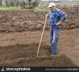 a tired worker is resting holding hie hand on a rake