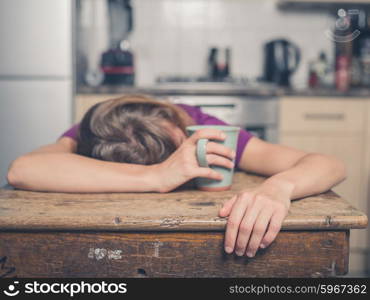 A tired young woman is having a cup of tea and is resting her head on a table