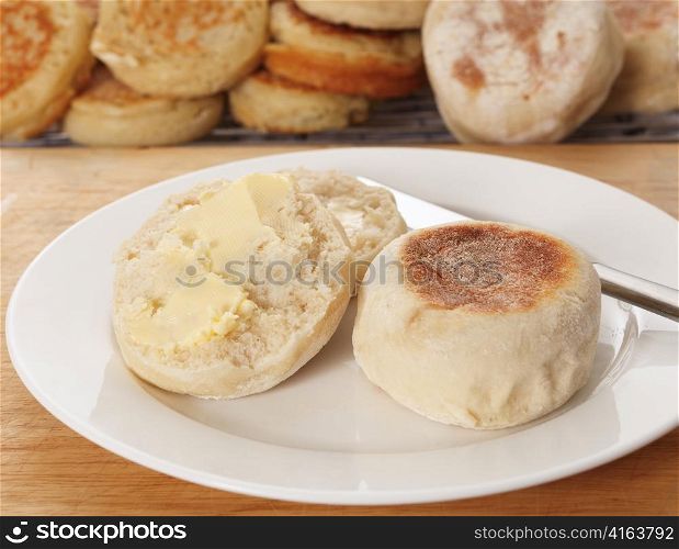 A traditional buttered English muffin tea-bread in front of a tray of fresh-baked home-made muffins and crumpets