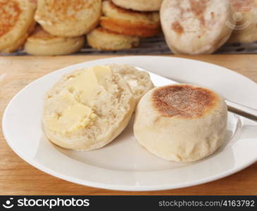 A traditional buttered English muffin tea-bread in front of a tray of fresh-baked home-made muffins and crumpets