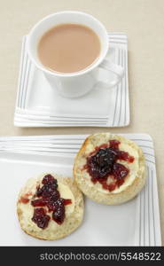 A traditional English afternoon tea of a scone topped with butter and blackcurrant jam and a cup of milky tea.