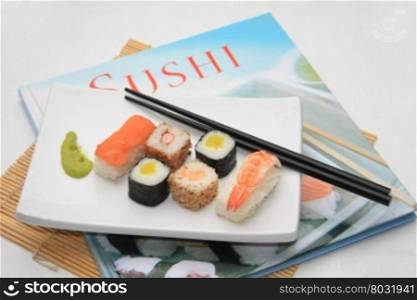 A traditional oblong Japanese plate with a variety of sushi on top of a Sushi book