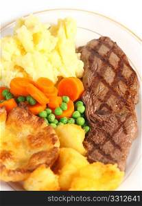 A traditional pub-grub style British meal of rump steak, mixed veg, mashed and roasted potatoes and Yorkshire pudding, viewed from above.