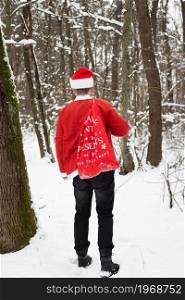 A traditional Santa Claus in a hat and a bag of gifts walks through the forest carrying gifts. Back view. A traditional Santa Claus in a hat and a bag of gifts walks through the forest carrying gifts. Back view.