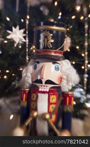 A traditional wooden nutcracker toy soldier playing a drum is a decoration in front of a Christmas Tree to provide some holiday spirit. A special lens effect blurs the outside of the image to add an element of dreaminess and separation from reality.