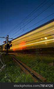 A train at full speed passing a railway crossing at dusk