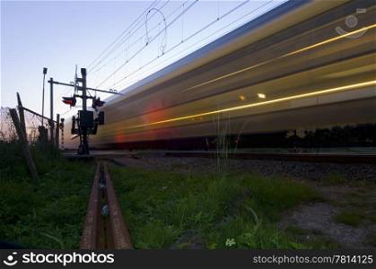 A train passing a railway intersection at hight speed just after dusk