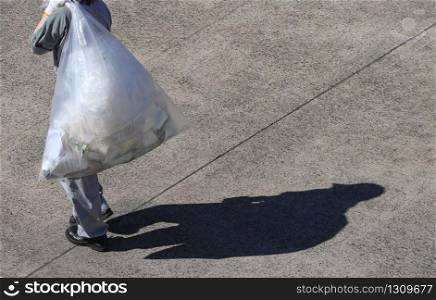 A trash keeping worker carrying a plastic trash bag on sunny day.