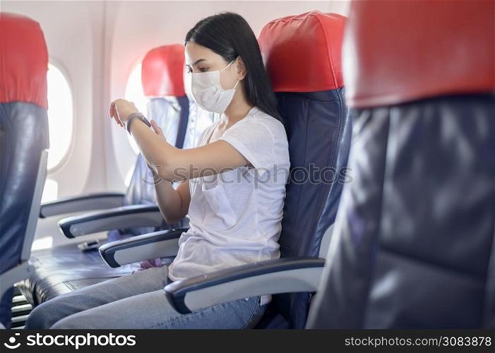 A traveling woman wearing protective mask onboard in the aircraft using smart watch, travel under Covid-19 pandemic, safety travels, social distancing protocol, New normal travel concept. Traveling woman wearing protective mask onboard in the aircraft using smart watch, travel under Covid-19 pandemic, safety travels, social distancing protocol, New normal travel concept