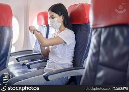 A traveling woman wearing protective mask onboard in the aircraft using smart watch, travel under Covid-19 pandemic, safety travels, social distancing protocol, New normal travel concept. Traveling woman wearing protective mask onboard in the aircraft using smart watch, travel under Covid-19 pandemic, safety travels, social distancing protocol, New normal travel concept