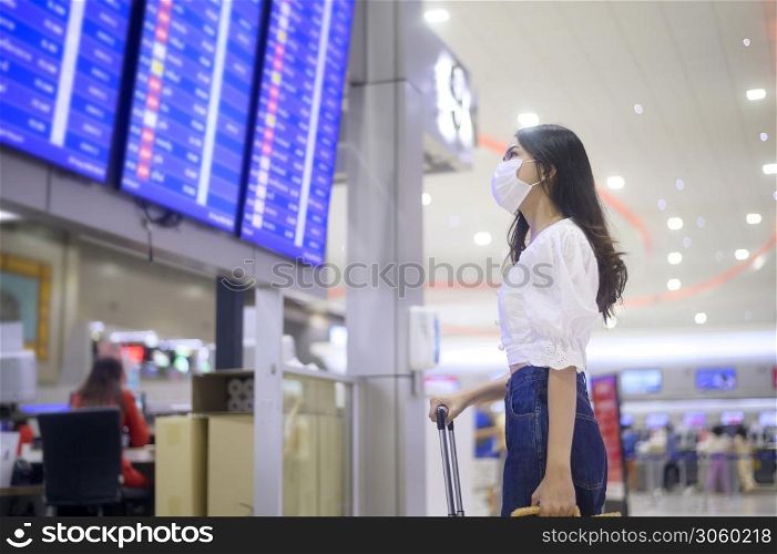 A traveller woman is wearing protective mask in International airport, travel under Covid-19 pandemic, safety travels, social distancing protocol, New normal travel concept