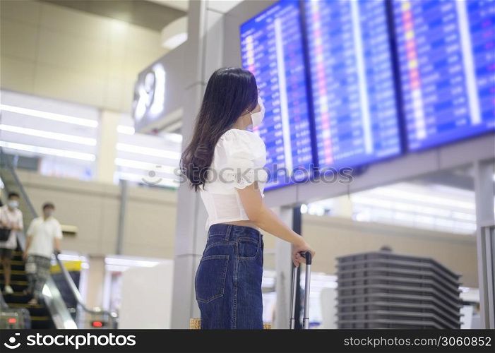 A traveller woman is wearing protective mask in International airport, travel under Covid-19 pandemic, safety travels, social distancing protocol, New normal travel concept