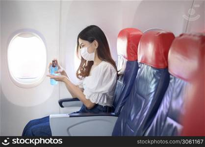 A travelling woman is wearing protective mask is washing hands with alcohol gel onboard in the aircraft, travel under Covid-19 pandemic, safety travels, social distancing protocol, New normal travel concept