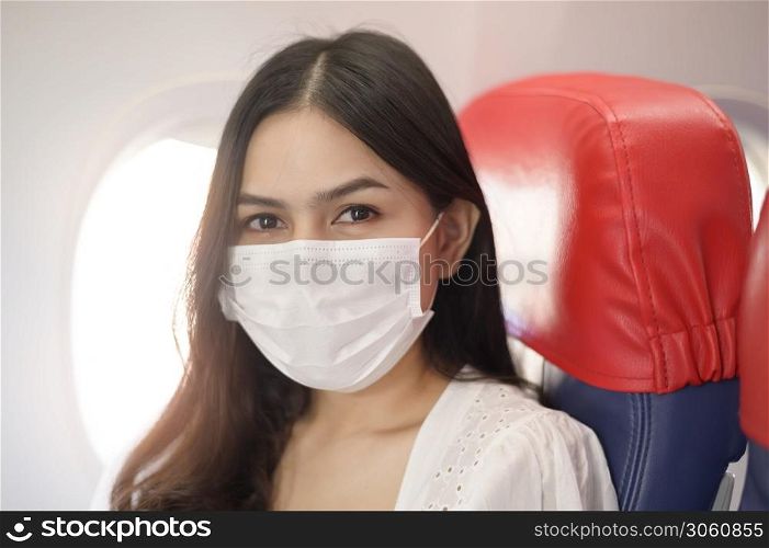 A travelling woman is wearing protective mask onboard in the aircraft, travel under Covid-19 pandemic, safety travels, social distancing protocol, New normal travel concept