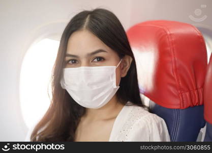 A travelling woman is wearing protective mask onboard in the aircraft, travel under Covid-19 pandemic, safety travels, social distancing protocol, New normal travel concept