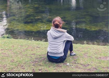 A trendy young woman is sitting by the water in a park
