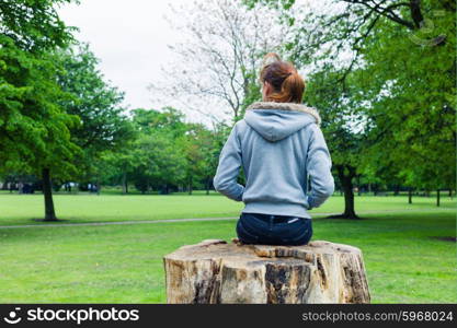 A trendy young woman is sitting on a tree trunk in the park