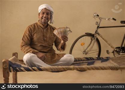 A TURBANED RURAL MAN HAPPILY HOLDING MONEY AND POSING IN FRONT OF CAMERA