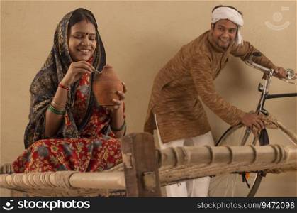 A TURBANED RURAL MAN LOOKING AT WIFE WHILE SHE PUTS MONEY IN PIGGY BANK