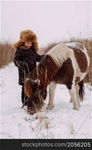 A two-colored pony and a child walk through a snowy field.. A fun winter story of a girl and a pony 3087.