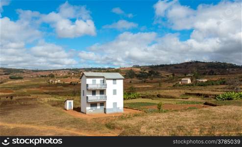 A two story white house next to a small white house in the middle of a beautiful landscape in Madagascar