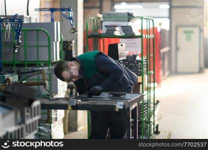 a uniformed worker working in a modern metal production and processing factory assembles parts of a new machine on his desk. High quality photo. a uniformed worker working in a modern metal production and processing factory assembles parts of a new machine on his desk