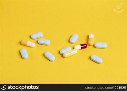 A variety of blue, yellow and red drugs and capsules against a yellow background.. A variety of blue, yellow and red pills and capsules against a yellow background.