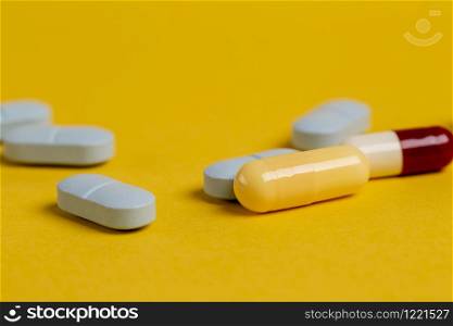 A variety of blue, yellow and red drugs and capsules against a yellow background.. A variety of blue, yellow and red pills and capsules against a yellow background.