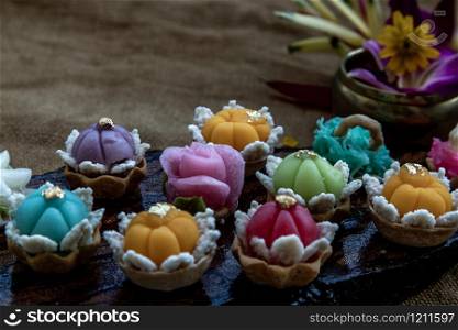 A variety of elegantly beautiful Thai Desserts (Khanom Wan Thai) colorful variations serving in a dark wooden, The bites in gold color and different flower shapes, Thai dessert, Auspicious dessert, Oblique view from the top.
