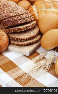 A variety of freshly baked breads along with three stocks of wheat. Shallow depth of field.