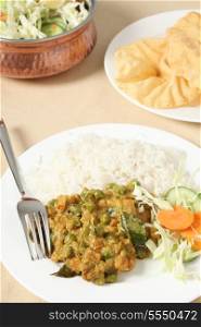 A vegetarian Indian meal of vegetable korma, rice and salad with poppadom crisps.
