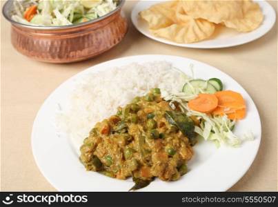 A vegetarian Indian meal of vegetable korma, rice and salad with poppadom crisps.