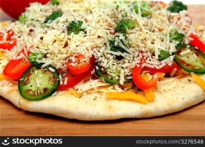 A veggie pizza ready to go into the oven topped with sharp cheddar and asiago cheese, fresh tomatoes, red bell pepper, mild jalapeno chilie, broccoli and dried herbs. Uncooked Vegtable Pizza For One