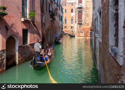 A Venetian gondolier in a traditional black gondola floats down a sunlit canal.. Venice. Gondolier in a traditional gondola on a sunny morning.