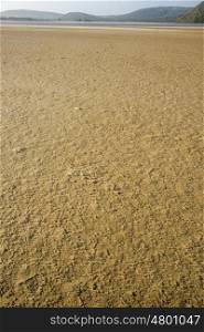 A vertical image of textured sea sand leading out to the river mouth in the distance.