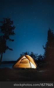 A vertical shot of a camping tent near trees during nighttime. Vertical shot of a camping tent near trees during nighttime