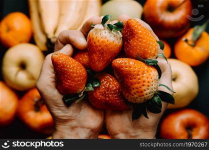 A vertical shot of two hands grabbing a bunch of strawberries over a bunch of vegetables