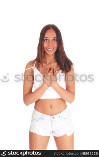 A very happy young woman standing from the front in shorts andwhite top with her hands on her chest, isolated for white background
