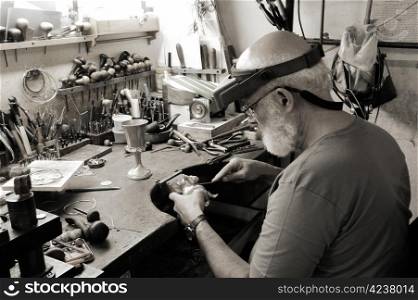 A very old jewelery shop and a jeweler handcrafting a silver dog and a cup. The style sepia photos.