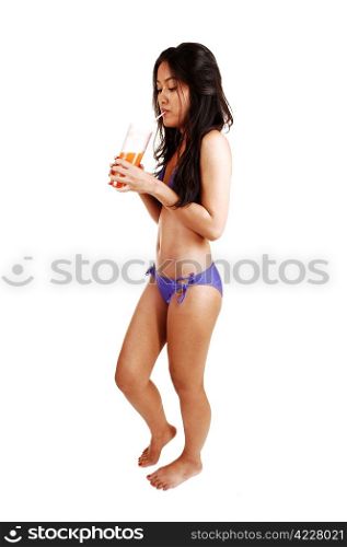 A very slim young Asian woman, with a glass of juice in her hand standingin her bikini and bare feet on white background.