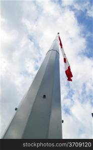 A very tall steel flag pole with a Canadian flag flying in the wind.