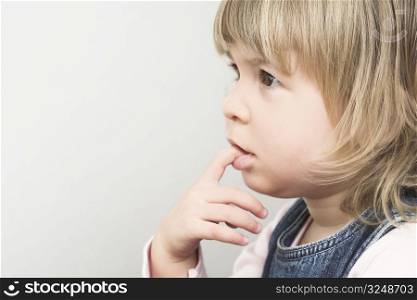 A very young, 18 months old girl is thinking with her little finger in her mouth.